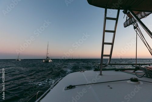 Many sailboats / catamarans in the distance sailing at sunset 