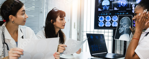 Team of female doctor check on scan results paper and looking at monitors in laboratory and plan and share medical knowledge and experience benefits her coworkers and patients