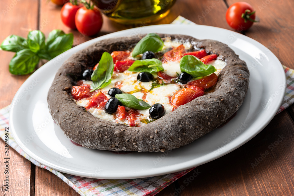 Deliziosa pizza con carbone vegetale e condita con mozzarella, pomodoro, olive, basilico e olio di oliva, cibo italiano