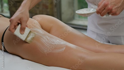 Preparation for massage: master masseur apply cream to hips and buttocks of a female client