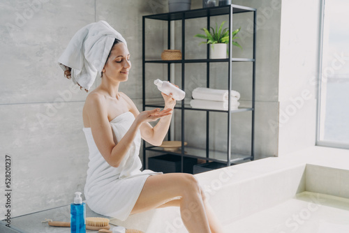 Female holding bottle of natural skincare cosmetics  moisturizing body after taking bath in bathroom