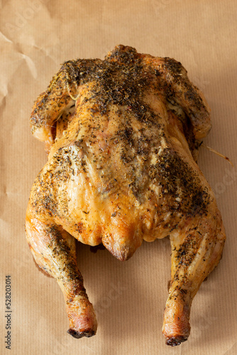 Whole chicken coated in mixed herbs roasted in an oven. On a brown paper background