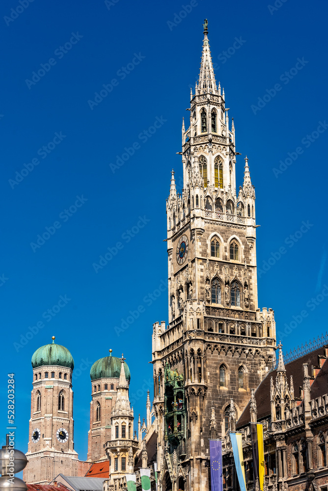 Die im Stil der Neugotik gestaltete Fassade des neuen Rathaus mit Rathausturm in der Altstadt von München in Unteransicht vom Marienplatz aus gesehen bei schönem Sommerwetter und blauen Himmel mit den