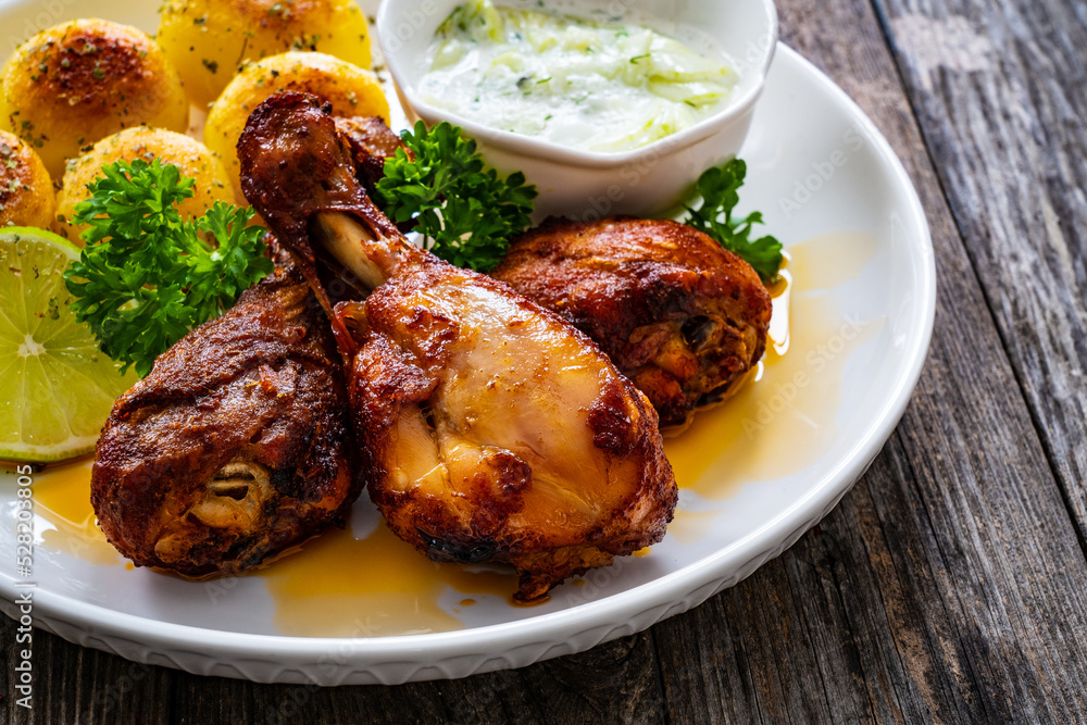 Roasted chicken drumsticks with fried potato and cucumbers in cream on wooden table

