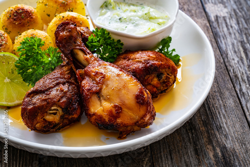 Roasted chicken drumsticks with fried potato and cucumbers in cream on wooden table