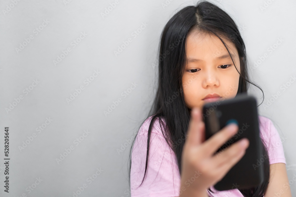 asian child or kid girl playing to looking smartphone or addicted mobile phone to hyperactive ADHD or young person study online and technology learning on white or gray wall background with copy space asian child or kid girl playing to looking smartphone or addicted mobile phone to hyperactive ADHD or young person study online and technology learning on white or gray wall background with copy space