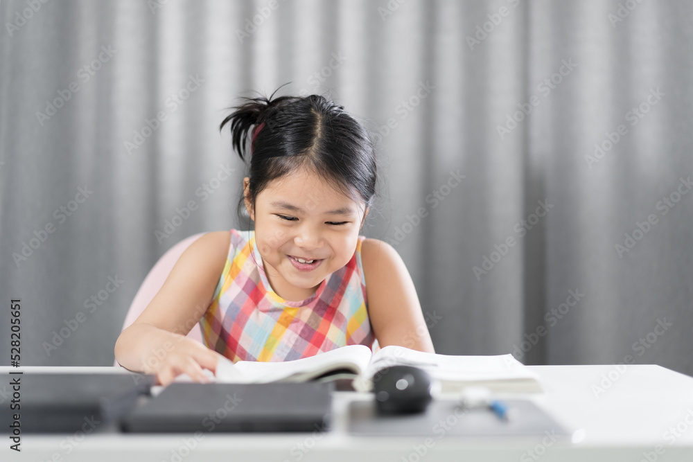 Asian child student or kid girl smile reading on book to learning and study online class with computer laptop or person happy fun learn from home to enjoy read on back to school studying by homeschool Asian child student or kid girl smile reading on book to learning and study online class with computer laptop or person happy fun learn from home to enjoy read on back to school studying by homeschool