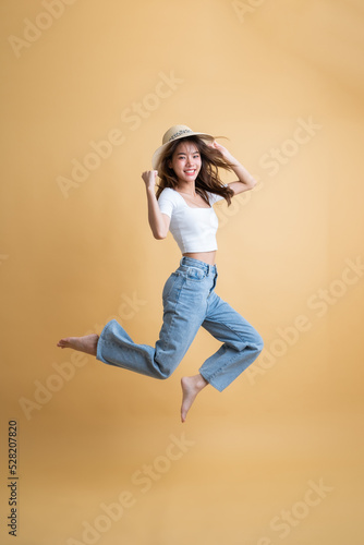 Fototapeta Naklejka Na Ścianę i Meble -  Full length of young attractive Asian woman traveler in casual clothes wearing straw hat with sunglasses jumping In Mid Air, Tourist girl having cheerful holiday trip concept
