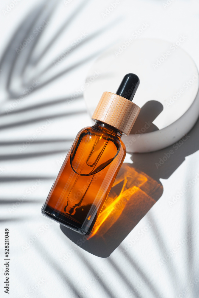 Naklejka premium Amber dropper bottles with serum, tonic or essential oil on concrete podium. White background with daylight with palm shadows. Beauty concept for face and body care