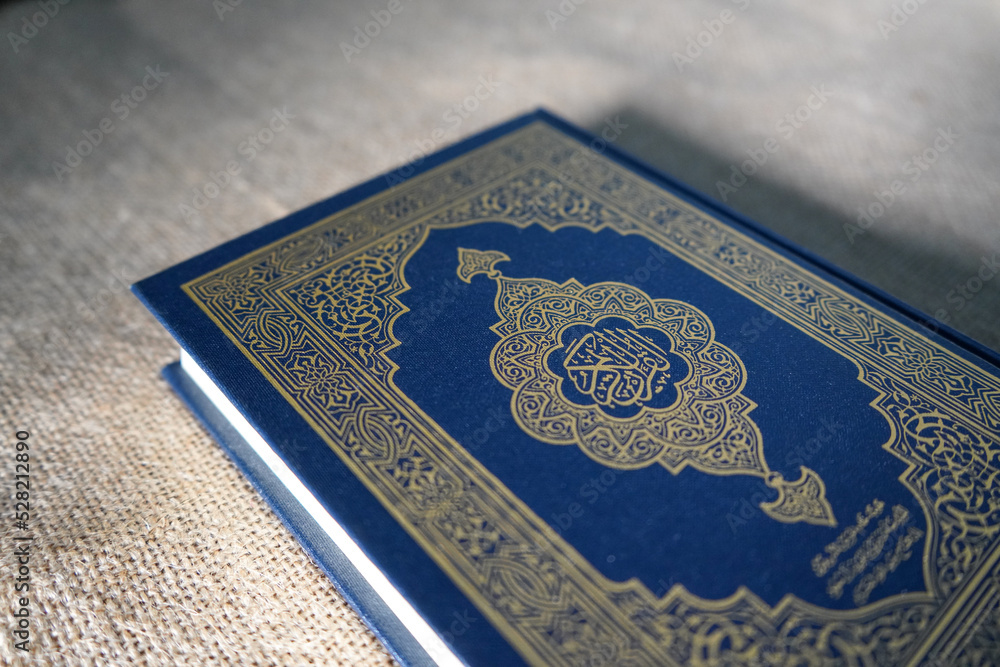 Fototapeta premium Indonesia - July, 2022 : The Quran, also romanized Qur'an or Koran, is central religious text of Islam, believed by Muslims to be revelation from God (Allah). Classical Arabic. Sack, blue.