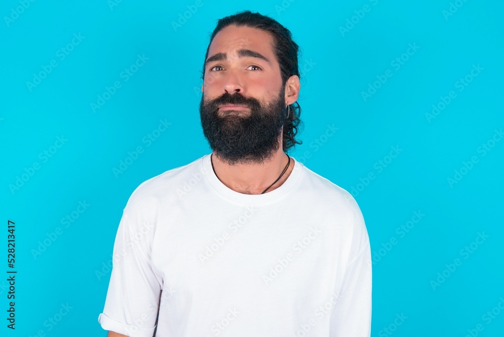 Fototapeta premium young bearded man wearing white T-shirt over blue studio background depressed and worry for distress, crying angry and afraid. Sad expression.