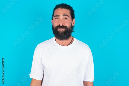 young bearded man wearing white T-shirt over blue studio background Pointing down with fingers showing advertisement, surprised face and open mouth © Roquillo