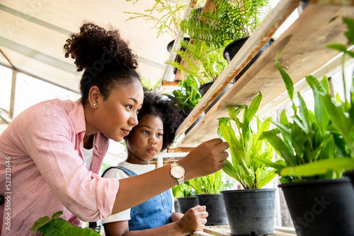 Africa American cute girl helping her mother to care for plants. Mom and her daughter engaging in gardening at garden. Happy family in spring day.