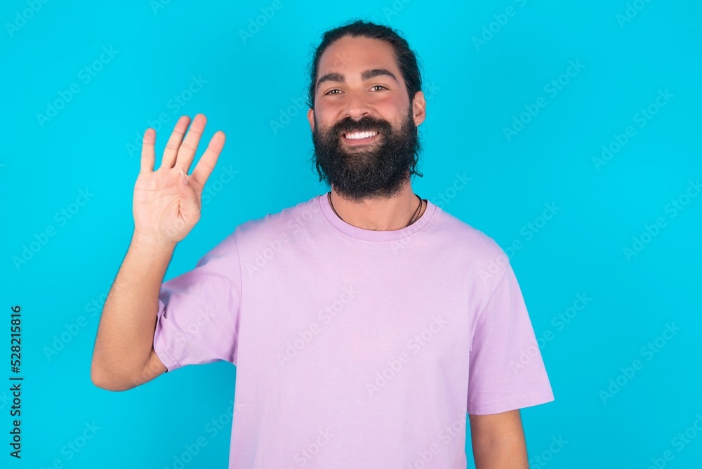 young bearded man wearing violet T-shirt over blue studio background showing and pointing up with fingers number four while smiling confident and happy. young bearded man wearing violet T-shirt over blue studio background showing and pointing up with fingers number four while smiling confident and happy.