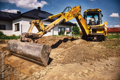 Excavator working at house construction site - digging foundations for modern house. Beginning of house building. Earth moving and foundation preparation.