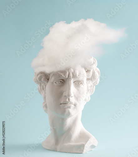 White plaster statue head of David with cloud  on pastel blue background. Minimal art poster. photo