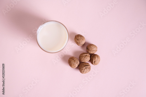 Still life with a raw vegan milk, alternative lactose free drink and organic wholesome walnuts on a pink background