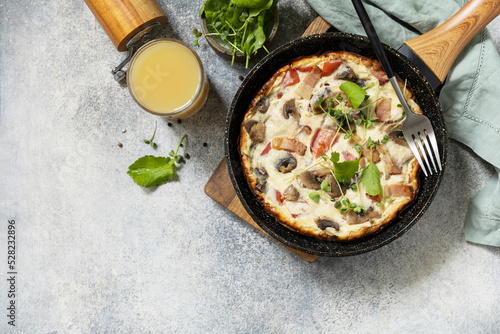 Italian breakfast dish. Rustic omelette (frittata) with mushrooms and bacon on a cast iron pan. View from above. Copy space.