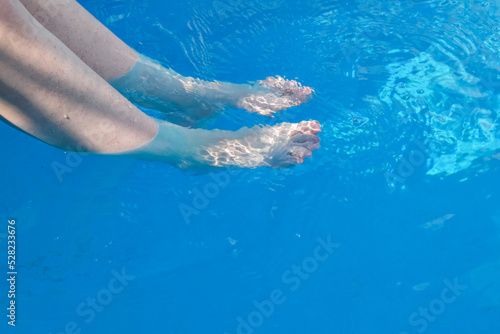Women s legs in the pool water. Barefoot and blue swimming pool wavy water background  great for your background and space for text