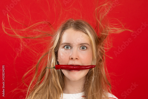 Shocked, expressed, surprised blonde woman with chili pepper in mouth and flying electrified hair locks. Copy space