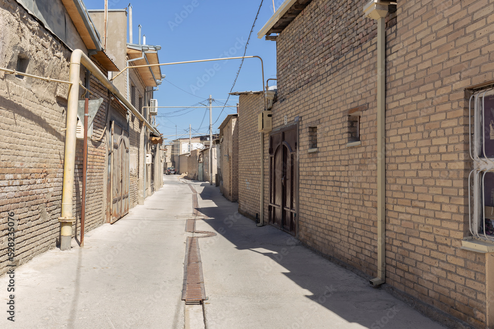 Residential area in old city with brick houses behind walls along narrow street, Bukhara, Uzbekistan