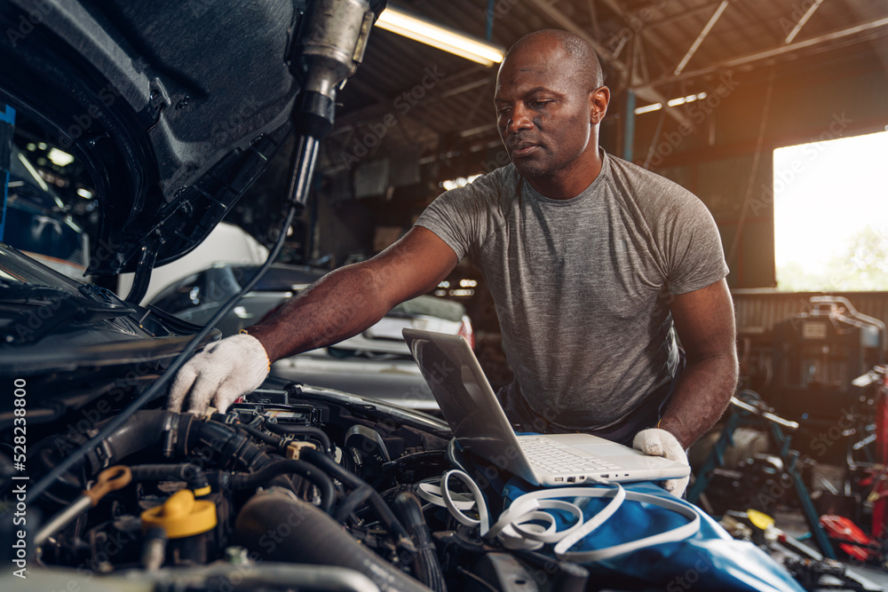 Man auto mechanic using laptop for checking and repair maintenance auto engine is problems at car repair shop.
