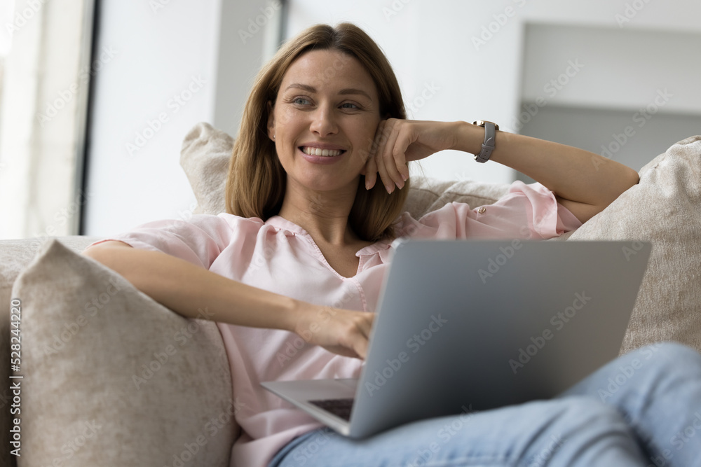 Happy joyful laptop user relaxing at home, resting on soft couch. Dreamy beautiful woman using computer on sofa, looking away, smiling thinking creative ideas. Online, Internet communication Happy joyful laptop user relaxing at home, resting on soft couch. Dreamy beautiful woman using computer on sofa, looking away, smiling thinking creative ideas. Online, Internet communication