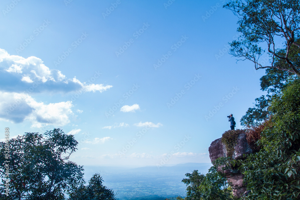 Green grass field on small hills and blue sky with clouds. Traveller stand on rock and take a picture of landscape.