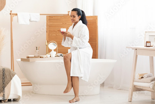 Mixed Woman Holding Moisturizer Cream Jar In Modern Bathroom