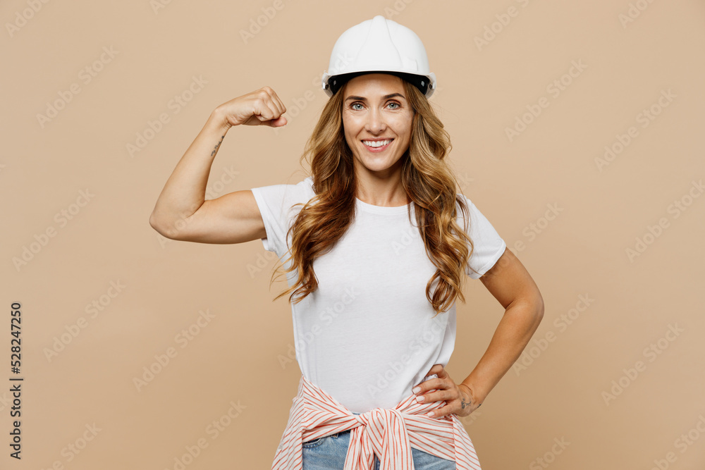 Young confident fun employee laborer handyman woman in white t-shirt helmet show hand muscles biceps isolated on plain beige background Instruments accessories for renovation room Repair home concept Young confident fun employee laborer handyman woman in white t-shirt helmet show hand muscles biceps isolated on plain beige background Instruments accessories for renovation room Repair home concept