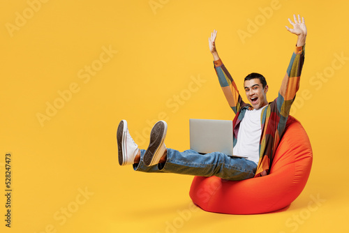 Full body young middle eastern man wear casual shirt white t-shirt sit in bag chair IT woman hold use work on laptop pc computer raise up hands finish job isolated on plain yellow background studio