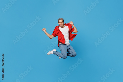 Full body young overjoyed excited cool man of African American ethnicity 20s wear red shirt jump high do winner gesture isolated on plain pastel light blue cyan background. People lifestyle concept