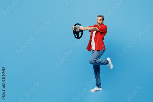 Full body young happy fun man of African American ethnicity 20s he wearing red shirt hold steering wheel pretend driving isolated on plain pastel light blue cyan background. People lifestyle concept.