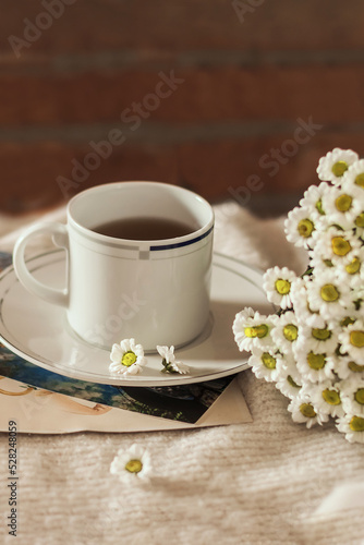 Morning coffee in the interior. Cozy composition  a cup of coffee with a saucer on a warm sweater and a bouquet of wild flowers against a brick wall. Still life concept. Copy space.