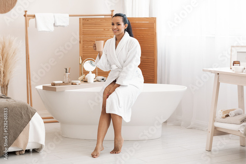 Happy Mixed Woman Drinking Coffee Enjoying Selfcare In Modern Bathroom