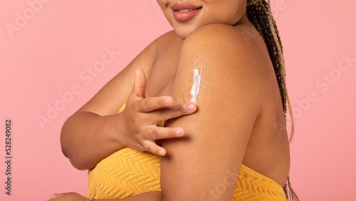 Unrecognizable Overweight Black Female Applying Moisturizer On Arm, Pink Background