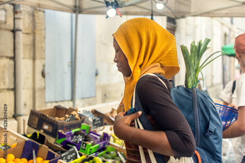 Young Black Muslim woman in hijab buying vegetables on a market street food, African Islamic lady with backpack outdoors Young Black Muslim woman in hijab buying vegetables on a market street food, African Islamic lady with backpack outdoors