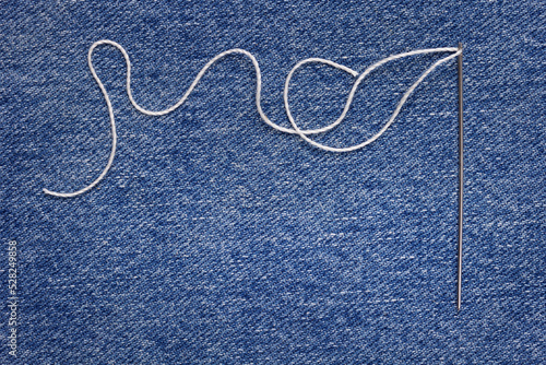 Sewing thread and needle at jeans denim background. Tailor texture handmade jeans concept