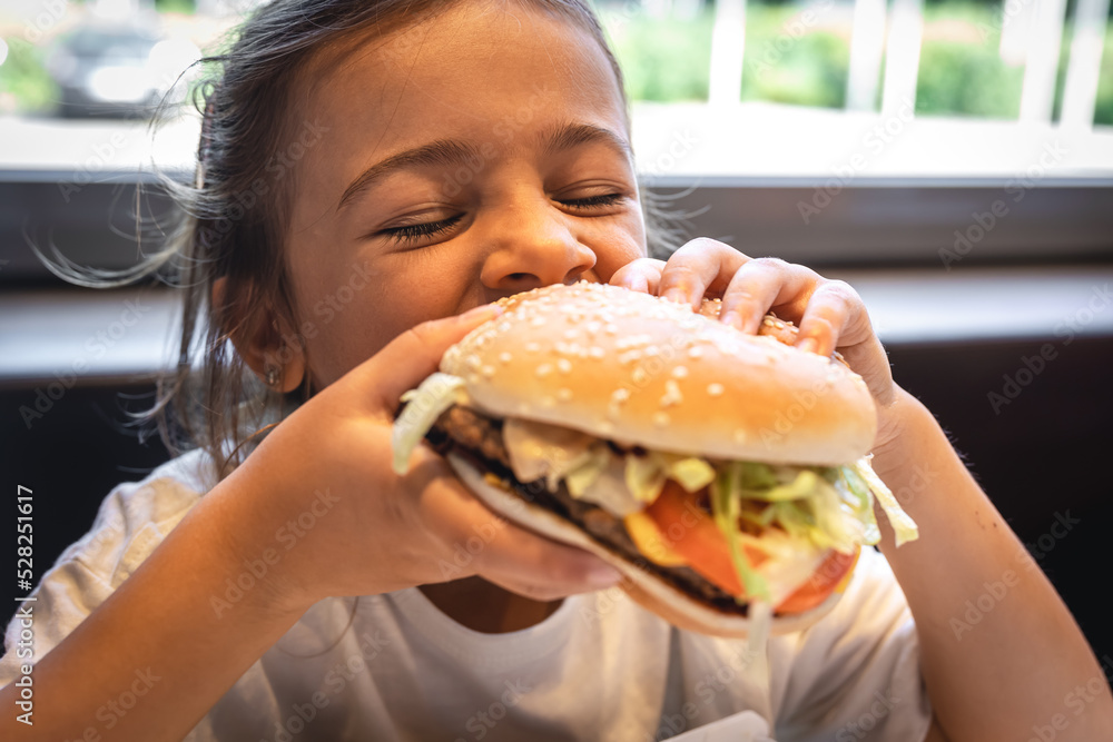 A little girl eats an appetizing burger, close-up. A little girl eats an appetizing burger, close-up.