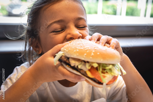 A little girl eats an appetizing burger  close-up.