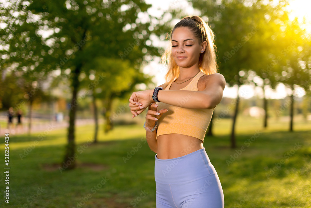 A woman with blue tights looking her smart watch in a public park in the morning A woman with blue tights looking her smart watch in a public park in the morning