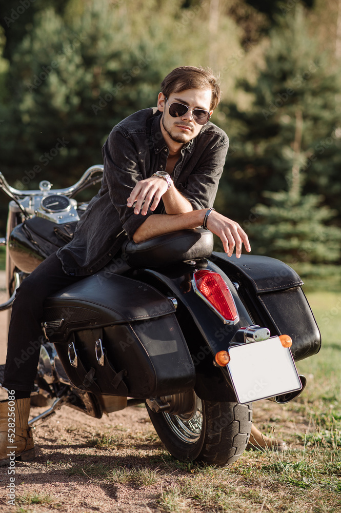 Young handsome male is sitting on his motor bike outdoors