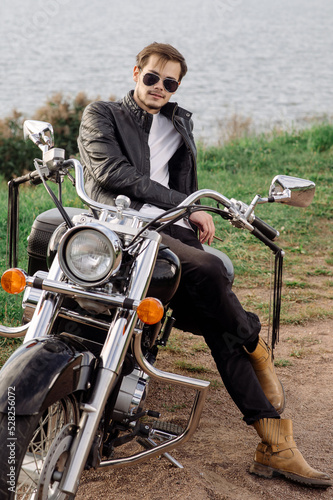 Young handsome male is sitting on his motor bike outdoors