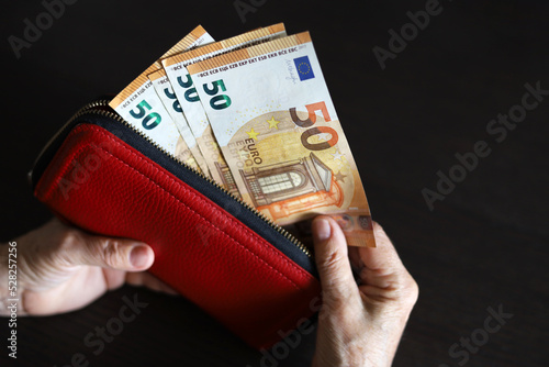 Fototapeta Naklejka Na Ścianę i Meble -  Elderly woman takes out euro banknotes from red wallet, selective focus on money, wrinkled female hands closeup. Concept of pension payments and assistance, savings, retirement in Europe