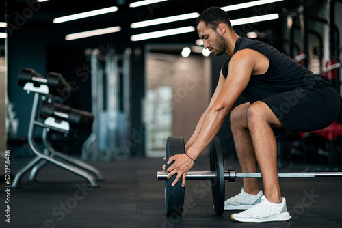 Young Black Male Athlete Adding Weight Plates On His Barbell At Gym