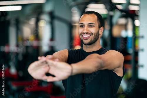 Happy Black Male Athlete Warming Up Before Training At Gym, Stretching Arms