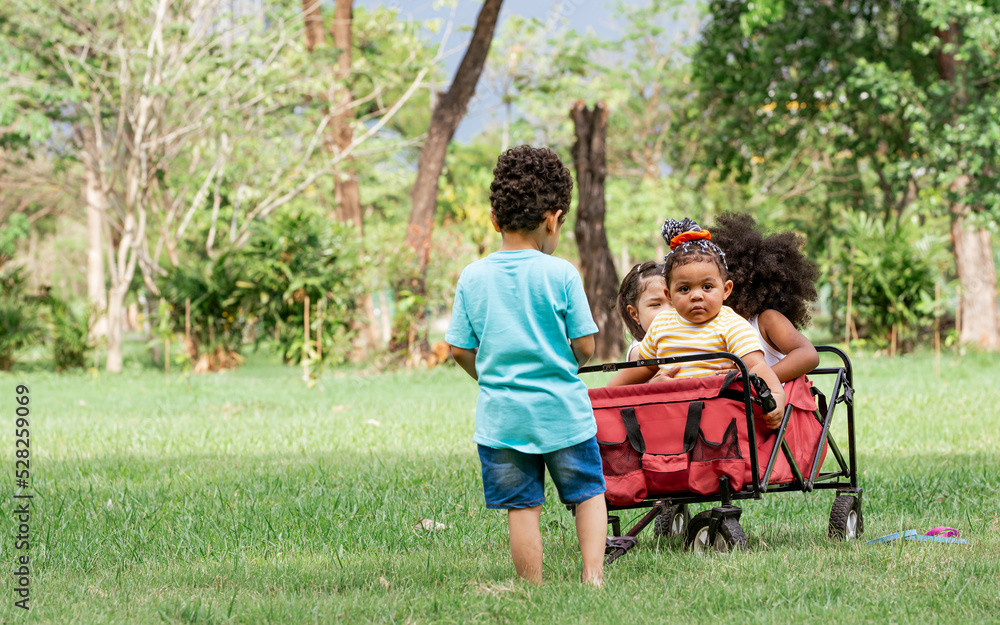 Obraz premium Mixed race little cute children pull and drag a red cart while playing in outdoor green park. Education, Diversity and Teamwork Concept.