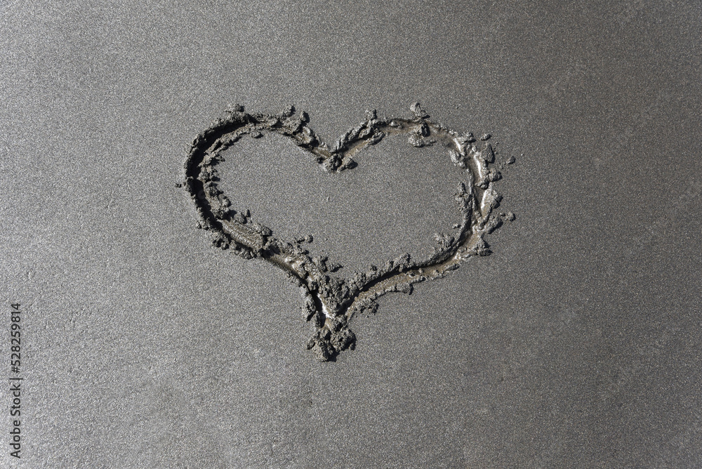 Drawing of a heart a sign of love on the gray sand of the beach