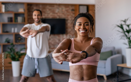 Happy young african american man and woman in sportswear doing stretching or warm up exercises