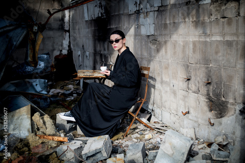 A girl dressed in black is drinking coffee in a destroyed cafe where a Russian army shell hit. photo